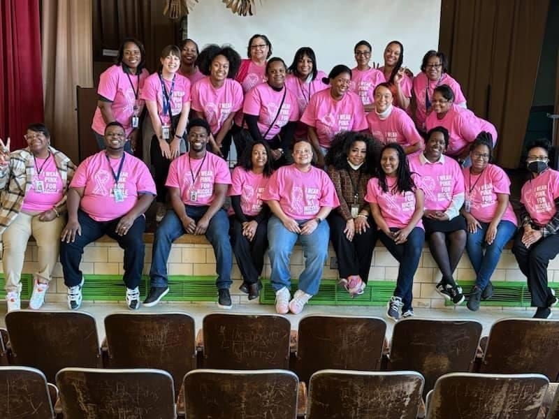 staff wearing pink shirts sitting on a stage